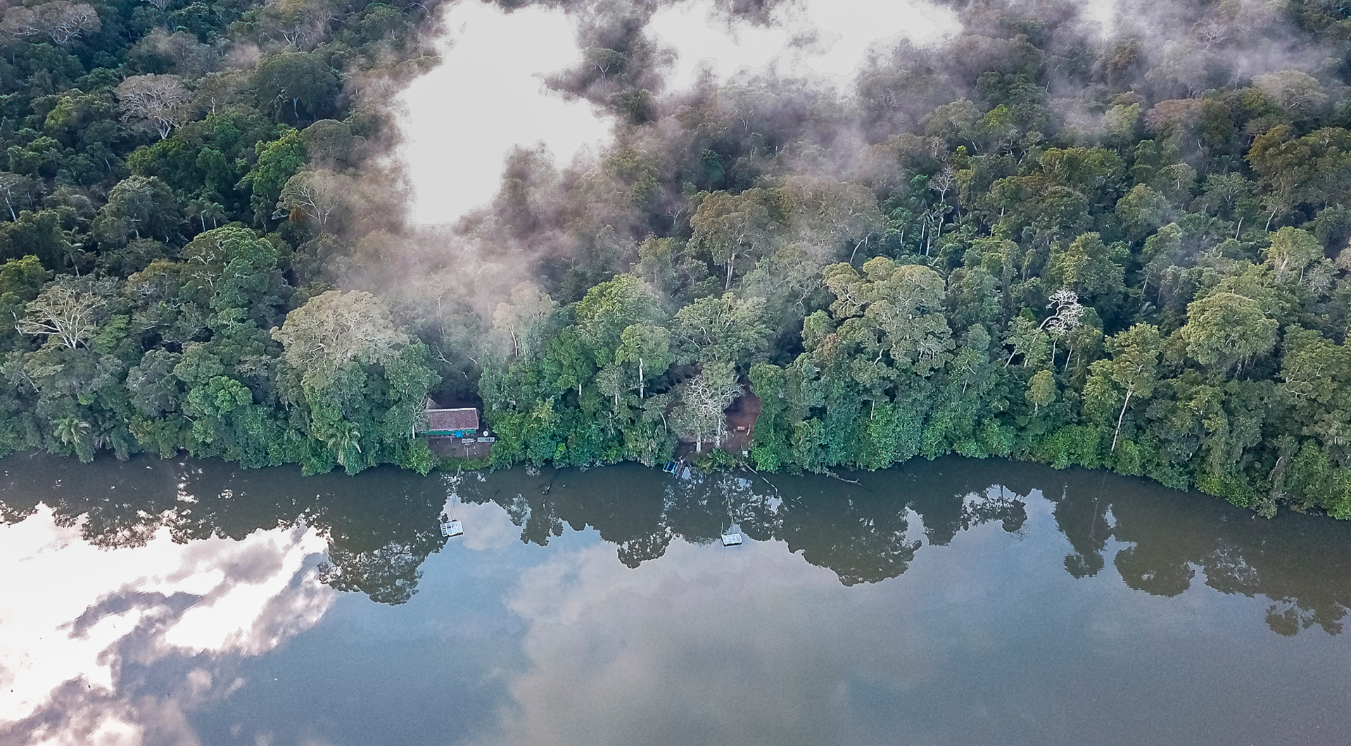 An aerial view of the amazon river with forest in the background and a small building.