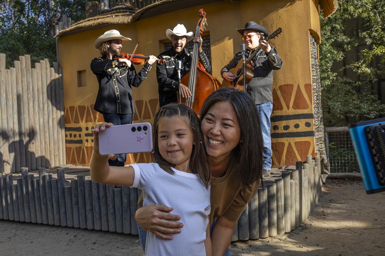 Child with adult snaps a selfie in front of an acoustic band.